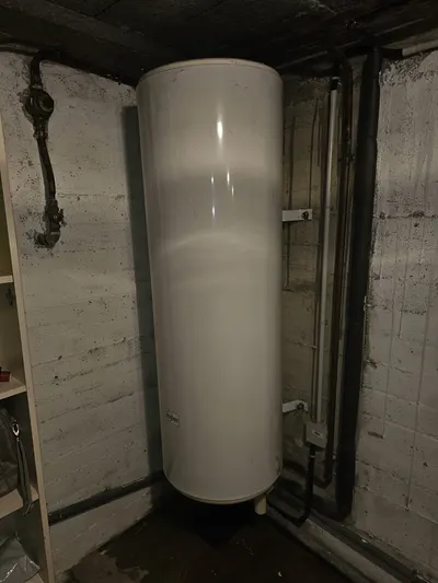 Ancien ballon d'eau chaude vertical dans un local sombre avant remplacement en urgence par AS Depann