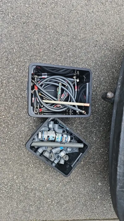 Bacs de flexibles, raccords et pièces PVC sortis du véhicule AS Depann sur le trottoir, matériel prêt pour une intervention chiffrée à l'avance
