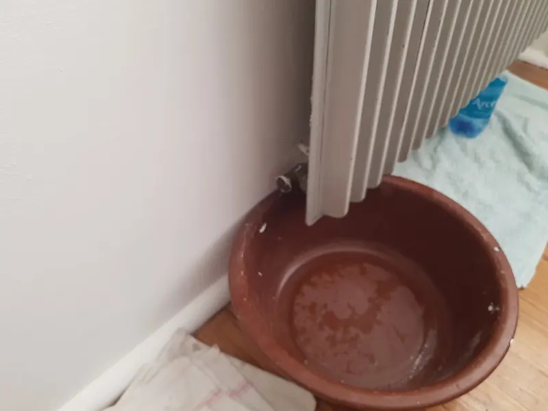 Bassine rouge placée sous un radiateur blanc pour récupérer une fuite, situation typique d'un dépannage de chauffage par AS Depann