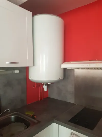 Chauffe-eau électrique blanc installé au mur d'une cuisine rouge au-dessus du plan de travail, pose AS Depann