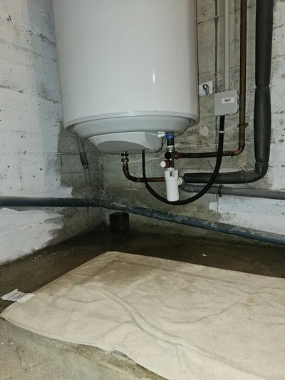 Chauffe-eau dans un sous-sol avec mur taché et sol humide, sinistre documenté par le plombier AS Depann pour l'assurance