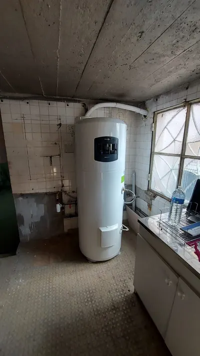 Chauffe-eau thermodynamique blanc installé dans une buanderie carrelée avec sa tuyauterie raccordée, pose AS Depann