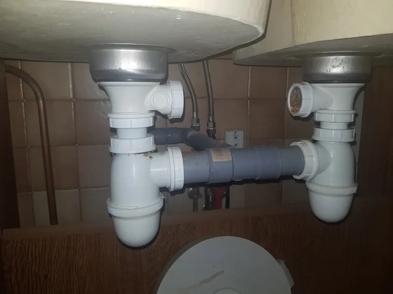 Double siphon PVC gris neuf sous un évier deux bacs, évacuation remontée par AS Depann après un débouchage d'évier de cuisine