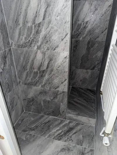 Douche carrelée marbre noir avec porte vitrée et radiateur sèche-serviettes, salle d'eau d'hôtes entretenue par AS Depann avant la saison