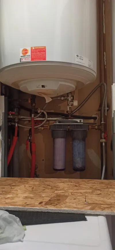 Filtre à eau double cartouche sous un chauffe-eau avec tuyauterie cuivre et vannes rouges, filtre en tête de réseau posé par AS Depann