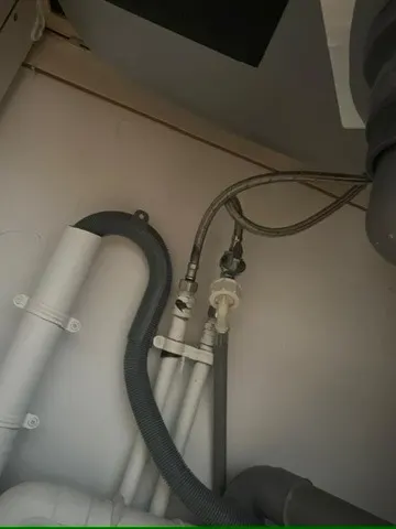 Flexibles et raccords sous un lavabo blanc avec siphon et alimentation, dessous d'un lave-mains de cabinet contrôlé par AS Depann
