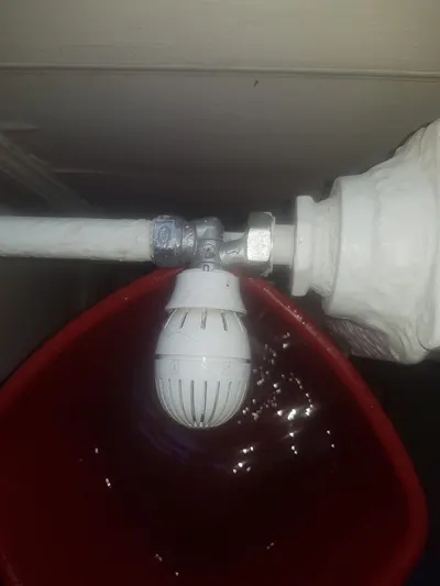 Groupe de sécurité de chauffe-eau démonté au-dessus d'un seau rouge lors d'un remplacement par AS Depann
