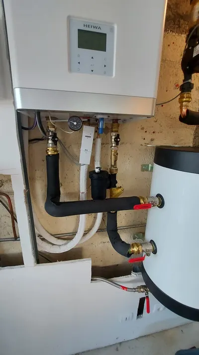 Local technique avec chaudière murale, chauffe-eau et tuyaux isolés noirs à vannes rouges, type de local où AS Depann installe un chauffe-eau thermodynamique