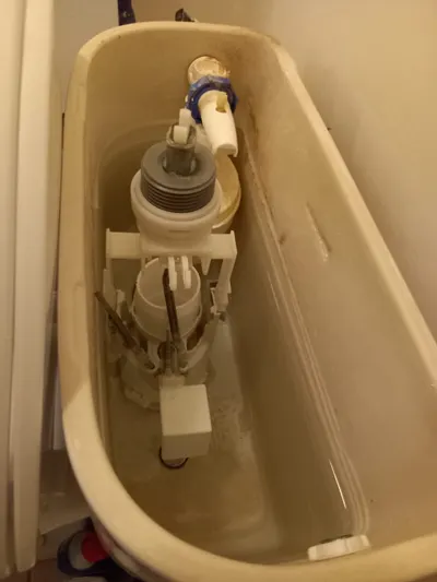 Mécanisme de chasse d'eau entartré à l'intérieur d'un réservoir de WC, cause typique d'une chasse qui coule en continu