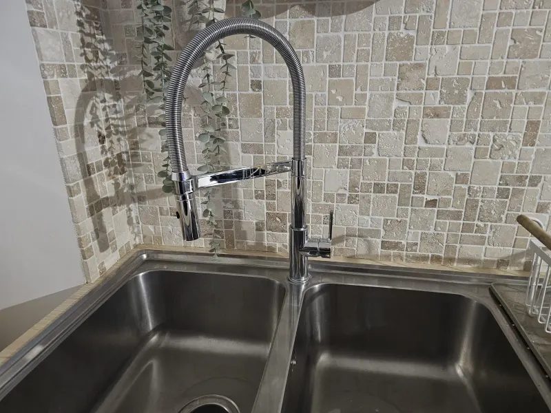 Mitigeur d'évier noir à douchette flexible installé sur un évier inox par AS Depann, exemple de remplacement de robinetterie