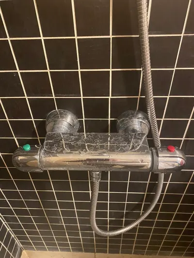 Mitigeur thermostatique de douche chromé entartré sur carrelage noir, panne de robinetterie typique de l'eau calcaire du sud de Lyon