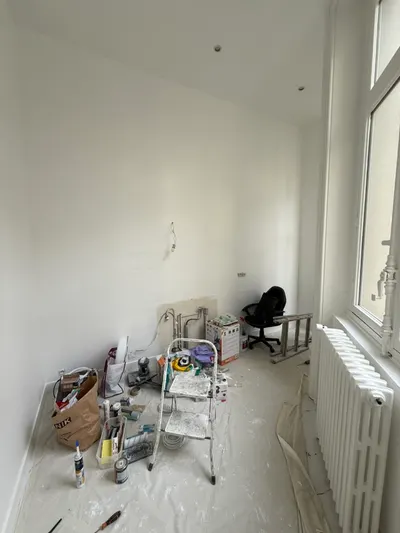 Pièce en rénovation avec radiateur, outils et matériaux au sol près de la fenêtre, remplacement de radiateur en cours de chantier par AS Depann