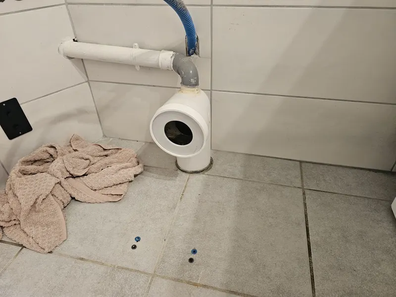 Pipe d'évacuation de WC déconnectée sur carrelage avec serpillière, en cours de remplacement, pipe fendue découverte lors d'un débouchage dans un immeuble ancien de Vienne