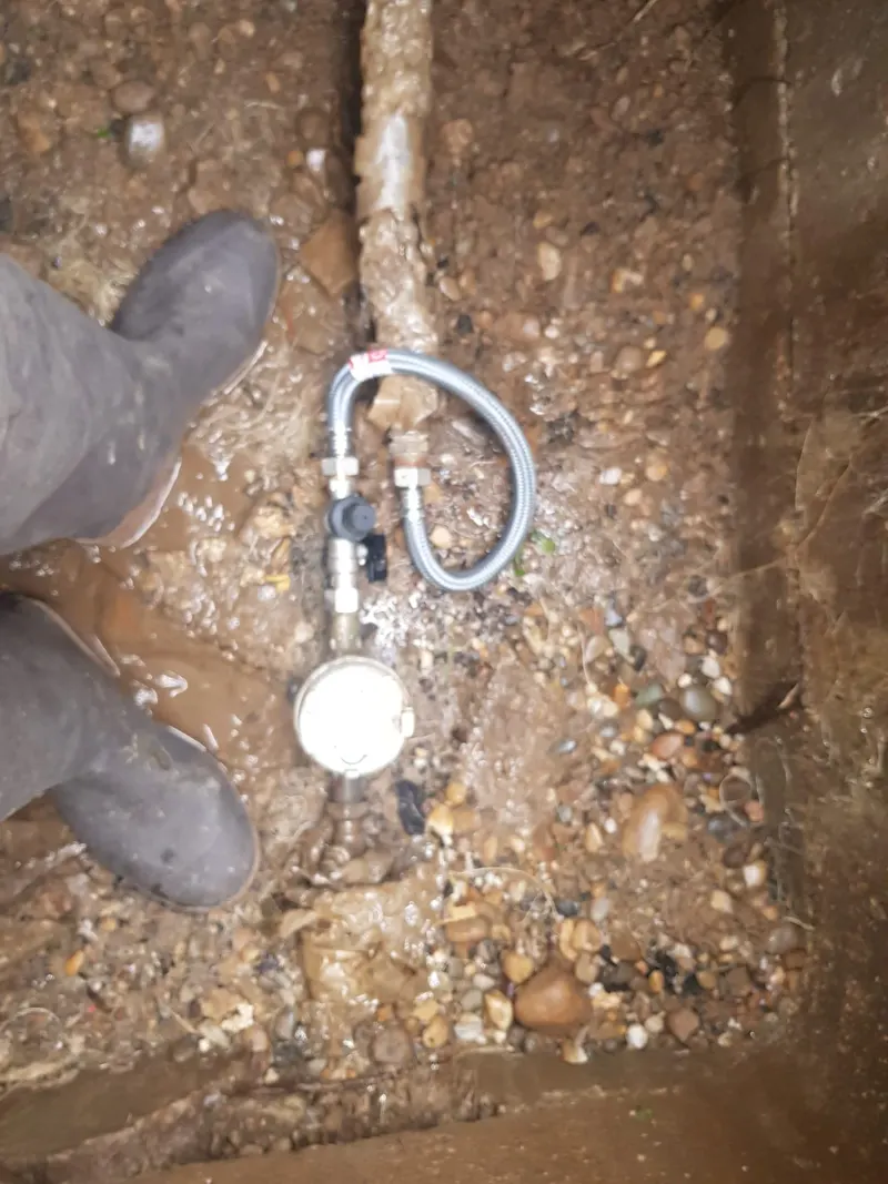 Raccord de compteur d'eau dégagé dans la terre au fond d'une tranchée après une recherche de fuite enterrée par AS Depann
