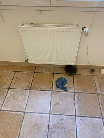 Radiateur acier blanc avec flaque d'eau sur carrelage beige et chiffon bleu, fuite de radiateur réparée par AS Depann