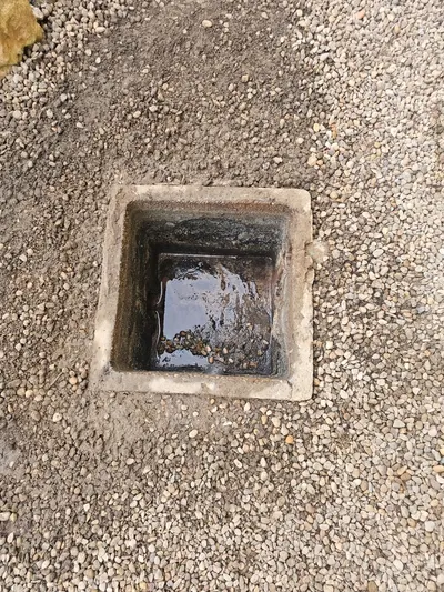 Regard carré ouvert dans un sol gravillonné extérieur avec canalisation au fond, accès à une canalisation extérieure bouchée traitée par AS Depann