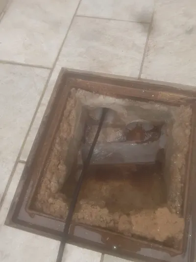 Regard d'évacuation ouvert dans un sol carrelé extérieur avec eau au fond, point d'accès pour un hydrocurage AS Depann