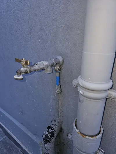Robinet extérieur laiton et vanne bleue sur canalisation d'eau le long d'un mur gris, robinet de jardin à purger avant l'hiver selon la checklist AS Depann contre le gel