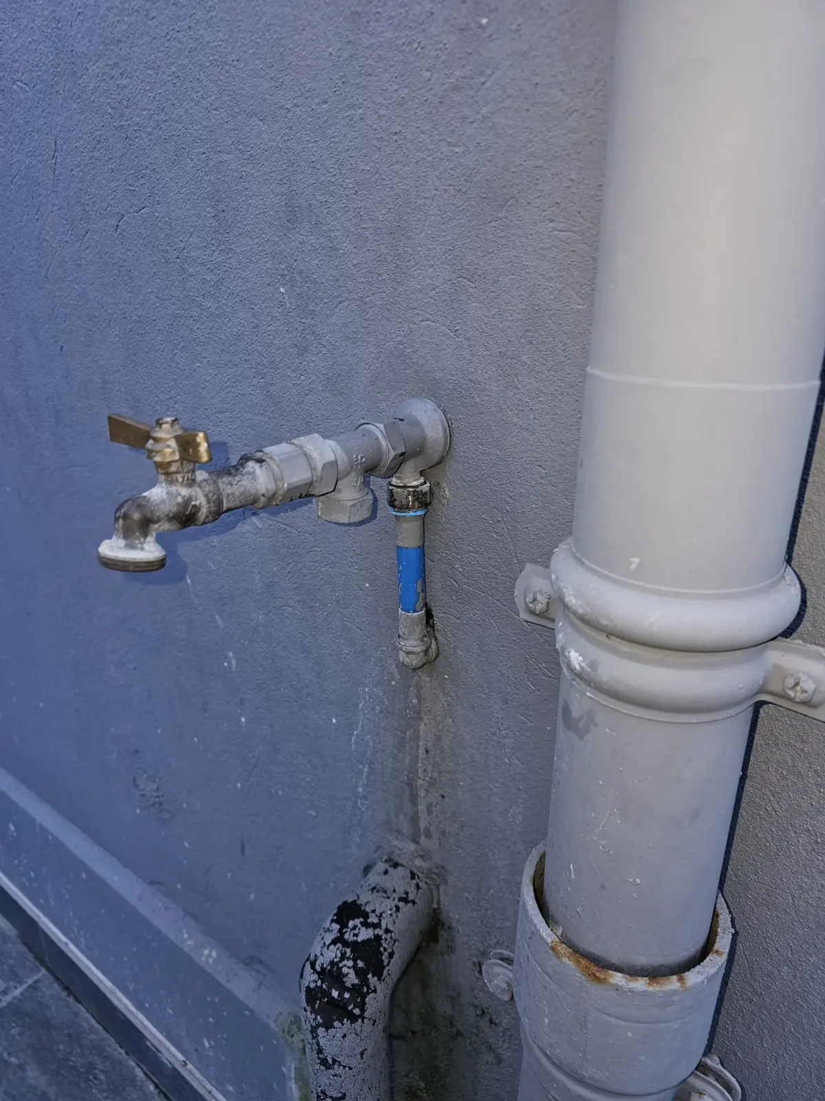Robinet de puisage extérieur et vanne d'arrêt le long d'une descente d'eau pluviale sur un mur, installation exposée au gel que AS Depann protège dans les maisons des monts du Lyonnais