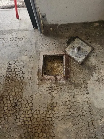 Siphon de sol ouvert dans un sol en béton fissuré de garage, point bas d'un sous-sol raccordé à un poste de relevage par AS Depann