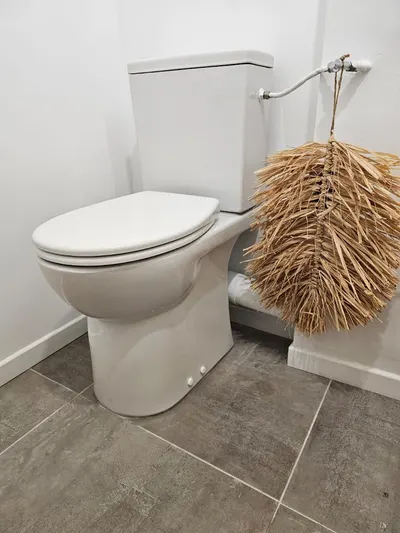 WC à poser blanc installé sur un sol carrelé gris avec brosse et décoration, remplacement de WC réalisé par AS Depann
