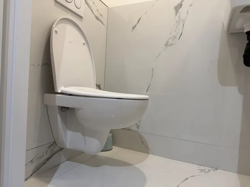 WC suspendu blanc installé contre un mur en carrelage marbre, bâti-support Geberit réparé par AS Depann sans casser l'habillage